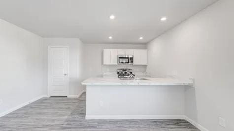 kitchen with white cabinetry, kitchen peninsula, appliances with stainless steel finishes, and light hardwood / wood-style flooring