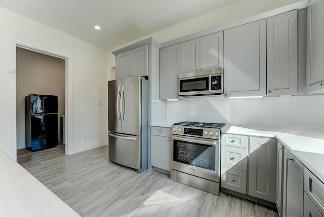 kitchen with decorative backsplash, appliances with stainless steel finishes, light hardwood / wood-style flooring, and gray cabinetry