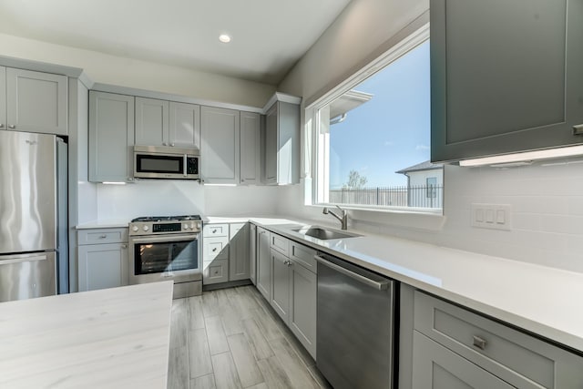 kitchen featuring appliances with stainless steel finishes, gray cabinets, light hardwood / wood-style floors, and sink