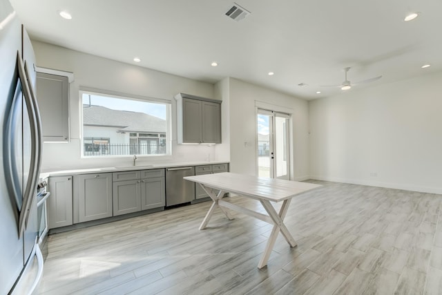 kitchen with gray cabinetry, stainless steel appliances, ceiling fan, sink, and light hardwood / wood-style floors