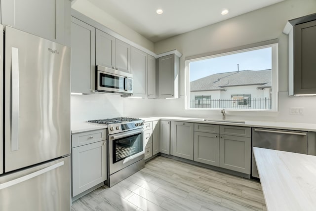 kitchen with appliances with stainless steel finishes, gray cabinets, light hardwood / wood-style floors, and sink