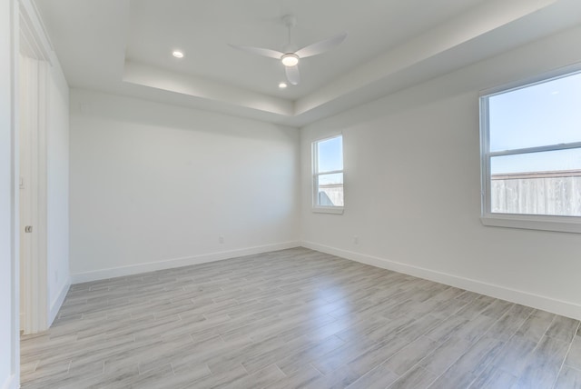 spare room with light wood-type flooring, a raised ceiling, and ceiling fan