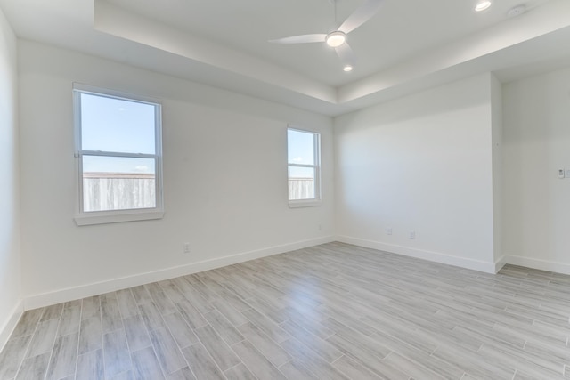 empty room with light wood-type flooring, a raised ceiling, and ceiling fan