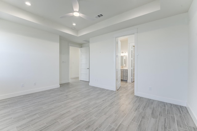 spare room with a raised ceiling, ceiling fan, and light hardwood / wood-style flooring