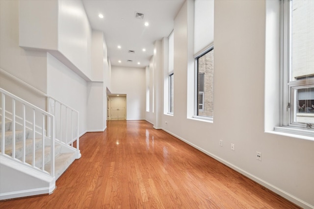 hallway featuring a healthy amount of sunlight, light wood-type flooring, and a towering ceiling