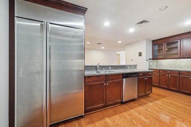 kitchen with backsplash, dark stone countertops, light wood-type flooring, and appliances with stainless steel finishes