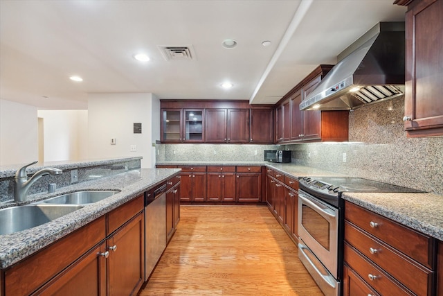 kitchen featuring light stone countertops, wall chimney exhaust hood, stainless steel appliances, sink, and light hardwood / wood-style flooring