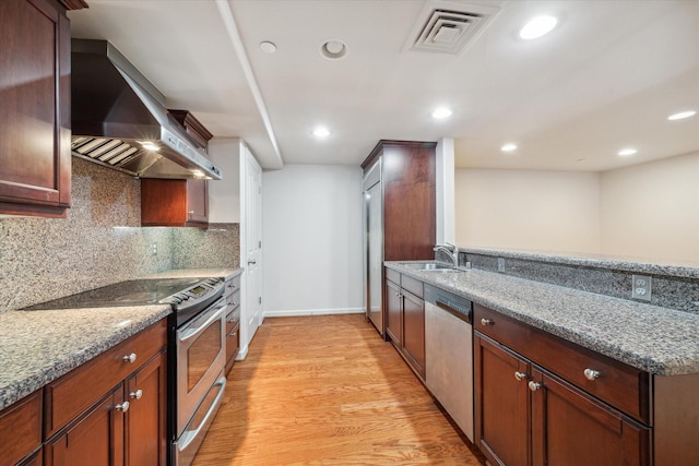 kitchen featuring stainless steel appliances, sink, wall chimney range hood, stone countertops, and light hardwood / wood-style floors