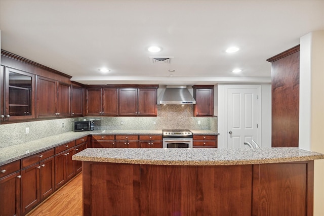 kitchen featuring electric range, wall chimney exhaust hood, light stone countertops, tasteful backsplash, and light hardwood / wood-style floors