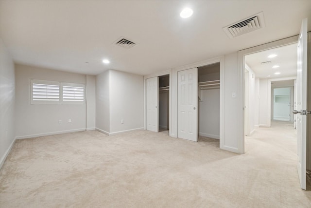 unfurnished bedroom featuring light carpet and two closets