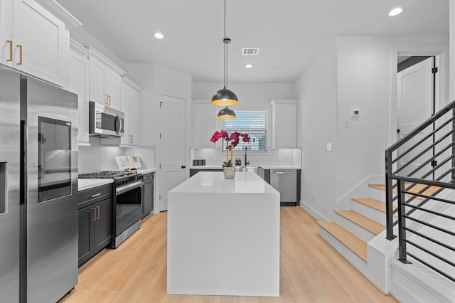 kitchen featuring white cabinets, appliances with stainless steel finishes, a center island, and decorative light fixtures