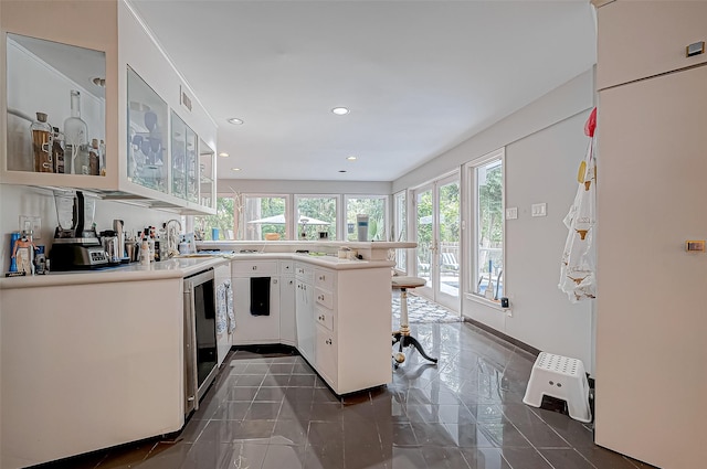 kitchen featuring recessed lighting, a peninsula, white cabinets, a kitchen breakfast bar, and glass insert cabinets