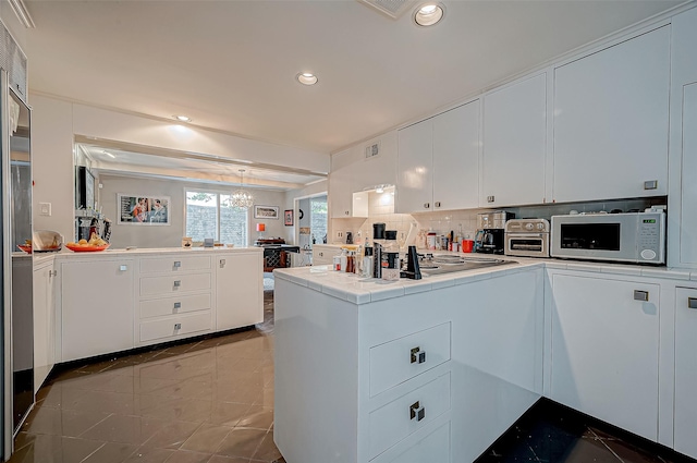 kitchen featuring tile countertops, white cabinets, backsplash, and kitchen peninsula