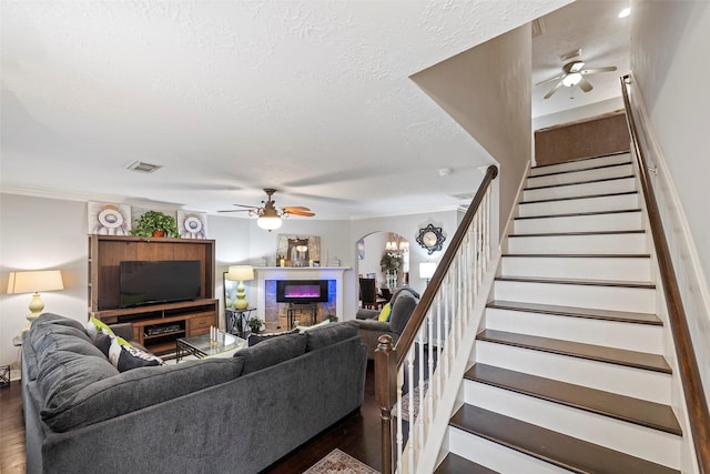 living room with a textured ceiling, ceiling fan, crown molding, and dark wood-type flooring