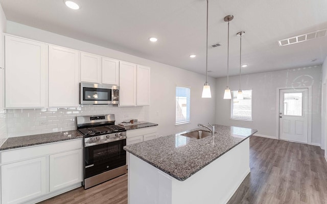 kitchen featuring visible vents, dark stone counters, appliances with stainless steel finishes, light wood-style floors, and a sink