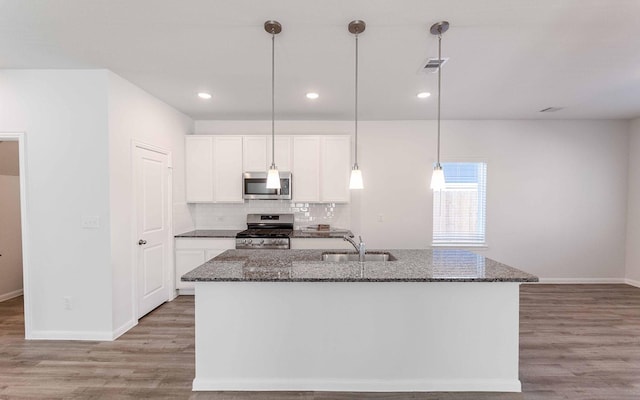 kitchen with stainless steel appliances, decorative backsplash, a sink, dark stone countertops, and light wood-type flooring