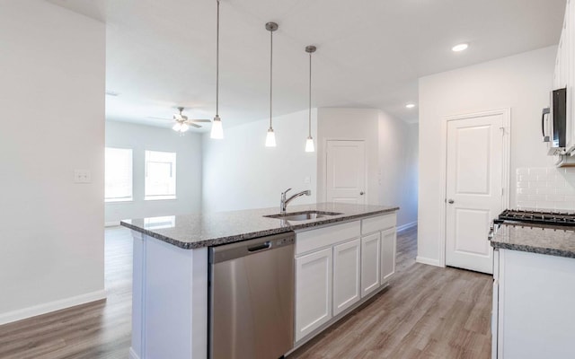 kitchen featuring light wood finished floors, stainless steel appliances, white cabinetry, a sink, and dark stone counters