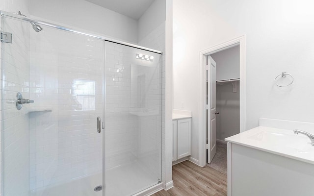 full bath featuring a shower stall, a spacious closet, wood finished floors, and vanity