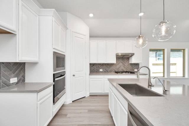 kitchen featuring sink, pendant lighting, light wood-type flooring, white cabinets, and appliances with stainless steel finishes