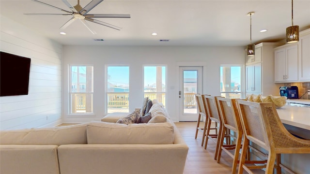 living room with ceiling fan, wooden walls, and light hardwood / wood-style flooring