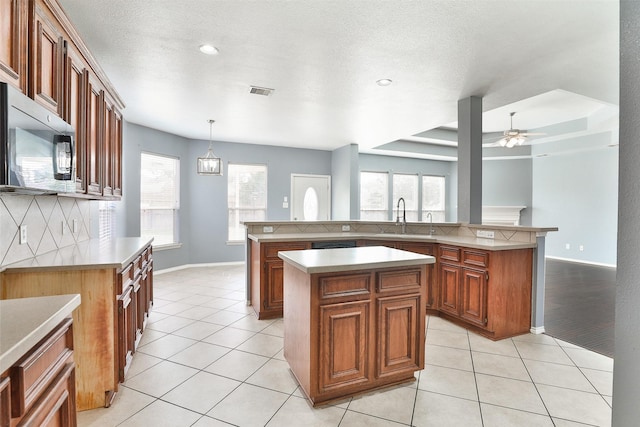 kitchen featuring ceiling fan with notable chandelier, pendant lighting, backsplash, and a kitchen island