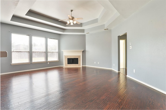 unfurnished living room featuring a raised ceiling, ceiling fan, dark wood-type flooring, and a tiled fireplace