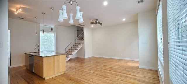 kitchen with light brown cabinetry, stainless steel dishwasher, a center island with sink, light hardwood / wood-style floors, and hanging light fixtures