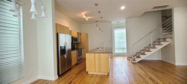 kitchen with sink, stainless steel appliances, decorative light fixtures, and light hardwood / wood-style flooring