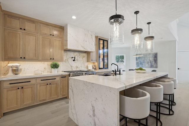 kitchen featuring pendant lighting, sink, light hardwood / wood-style flooring, a large island, and a kitchen bar