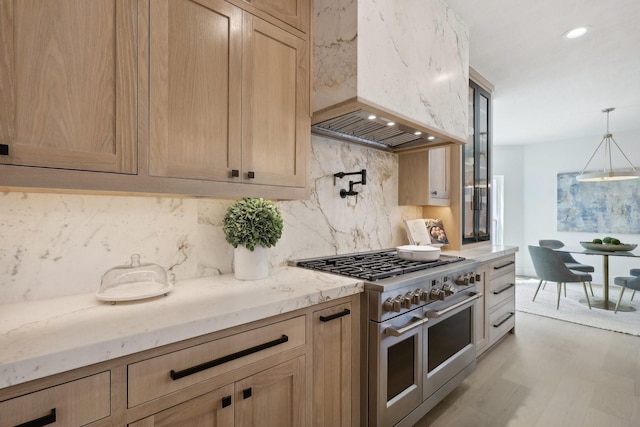 kitchen featuring range with two ovens, light brown cabinetry, decorative light fixtures, light hardwood / wood-style floors, and custom range hood