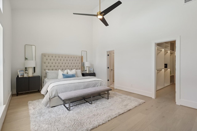 bedroom with ceiling fan, light hardwood / wood-style floors, a walk in closet, and high vaulted ceiling