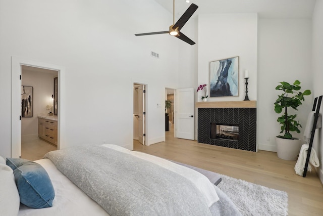 bedroom with light wood-type flooring, ensuite bathroom, ceiling fan, high vaulted ceiling, and a tiled fireplace