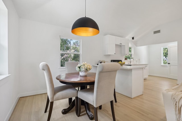 dining room with sink, plenty of natural light, vaulted ceiling, and light wood-type flooring