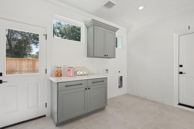 clothes washing area featuring electric dryer hookup, crown molding, light tile patterned flooring, and cabinets