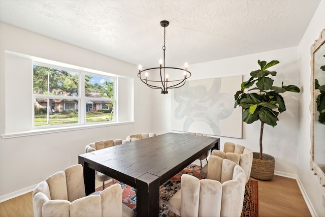 dining area with light hardwood / wood-style flooring, a textured ceiling, and a notable chandelier