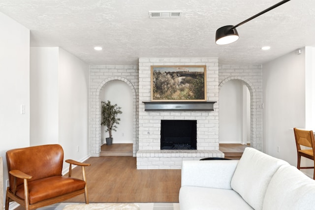 living room with hardwood / wood-style floors, a textured ceiling, and a brick fireplace