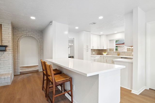 kitchen featuring white cabinetry, sink, kitchen peninsula, a breakfast bar area, and light wood-type flooring