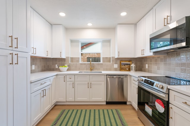 kitchen featuring decorative backsplash, light wood-type flooring, stainless steel appliances, sink, and white cabinets