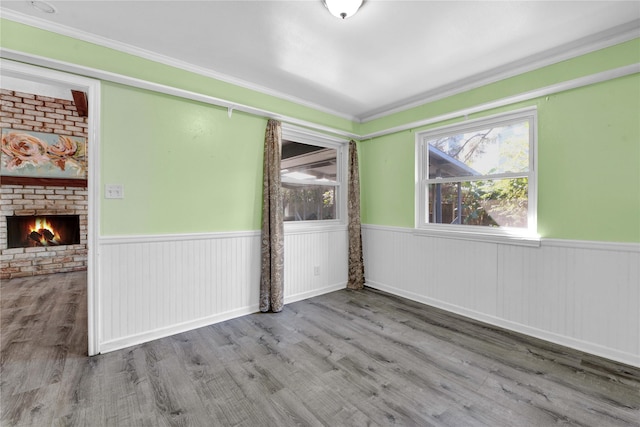 unfurnished room with hardwood / wood-style flooring, crown molding, and a brick fireplace