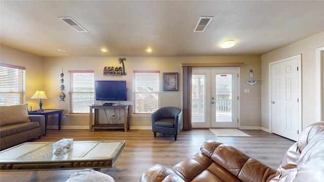 living room featuring a healthy amount of sunlight, french doors, a textured ceiling, and light hardwood / wood-style flooring