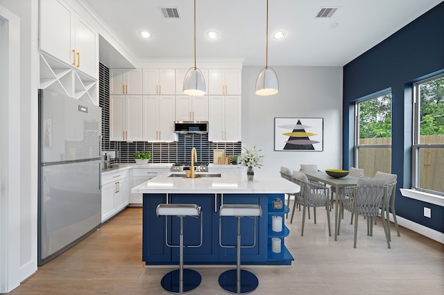 kitchen with a breakfast bar area, white cabinetry, hanging light fixtures, fridge, and an island with sink