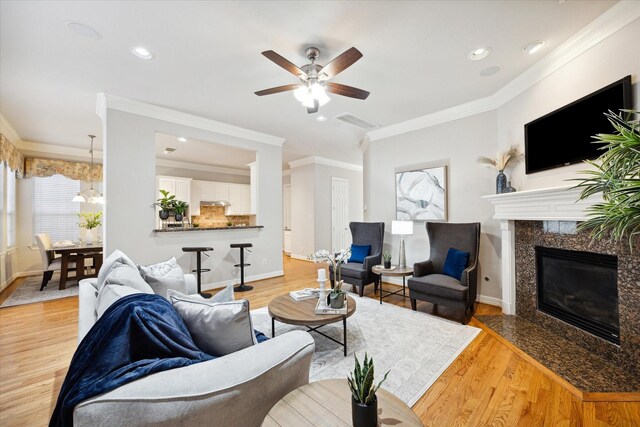 living room with ceiling fan, light wood-type flooring, crown molding, and a premium fireplace