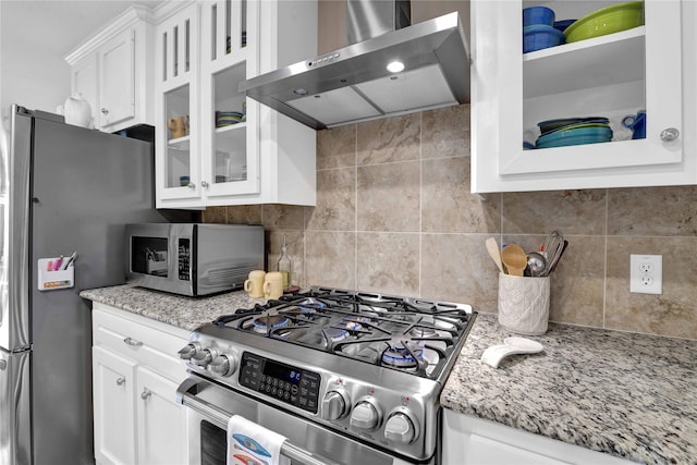 kitchen featuring decorative backsplash, appliances with stainless steel finishes, light stone countertops, wall chimney range hood, and white cabinets