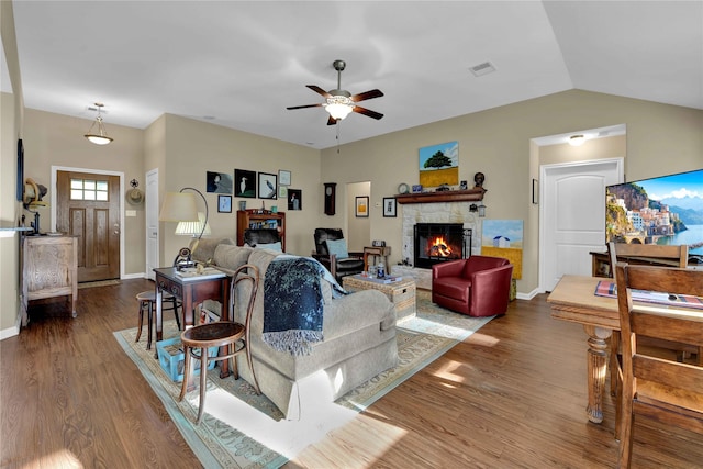 living room with hardwood / wood-style flooring, ceiling fan, a stone fireplace, and vaulted ceiling