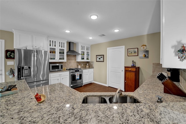 kitchen with wall chimney range hood, appliances with stainless steel finishes, light stone counters, and sink