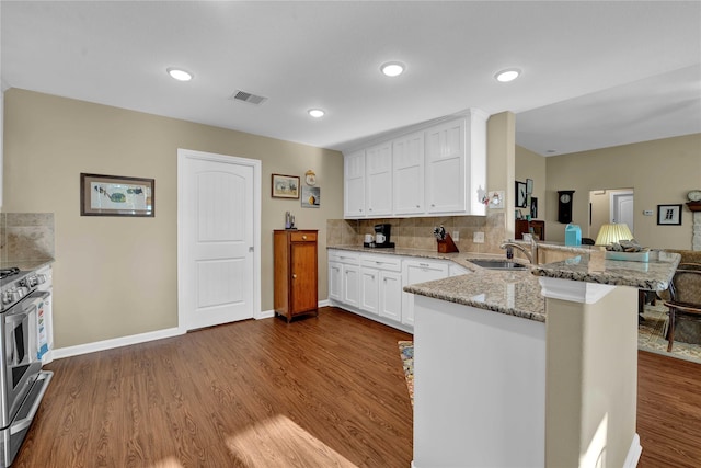 kitchen with kitchen peninsula, light stone counters, sink, white cabinets, and stainless steel range with gas stovetop