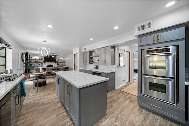 kitchen with double oven, light stone countertops, a center island, and light wood-type flooring