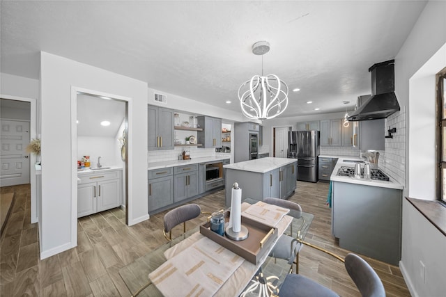 kitchen featuring pendant lighting, a center island, ventilation hood, appliances with stainless steel finishes, and tasteful backsplash