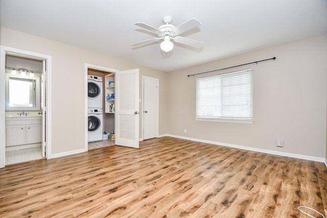 unfurnished bedroom featuring ensuite bathroom, sink, stacked washer and dryer, light hardwood / wood-style flooring, and ceiling fan