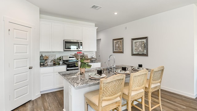 kitchen with light stone countertops, white cabinetry, stainless steel appliances, dark hardwood / wood-style floors, and a center island with sink